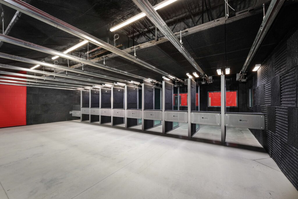 An indoor shooting range with a row of individual firing lanes against black sound-absorbing walls.