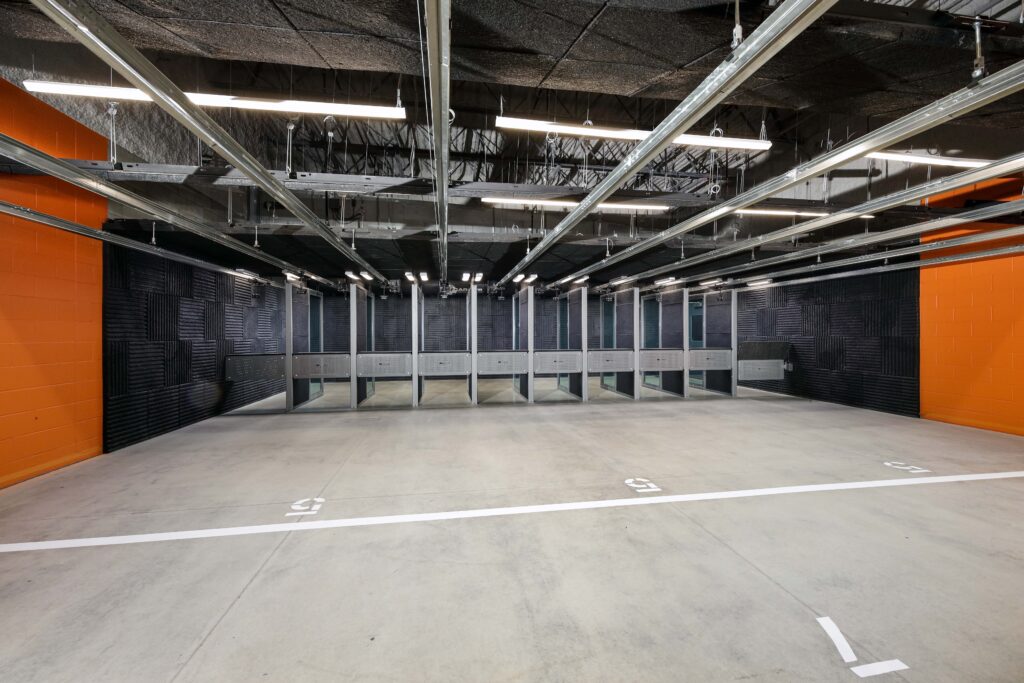 An indoor shooting range with numbered firing lanes, black sound-dampening walls, and orange side walls.