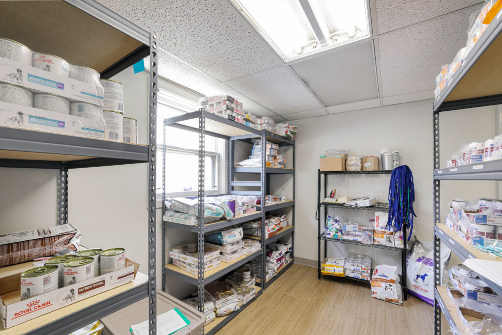 Shelves in a veterinary or pet supply storage room stocked with canned and bagged pet food and medical supplies.