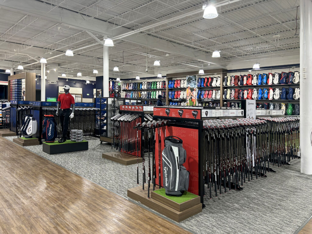 Interior of a golf shop featuring rows of golf clubs and golf bags displayed on shelves and racks.