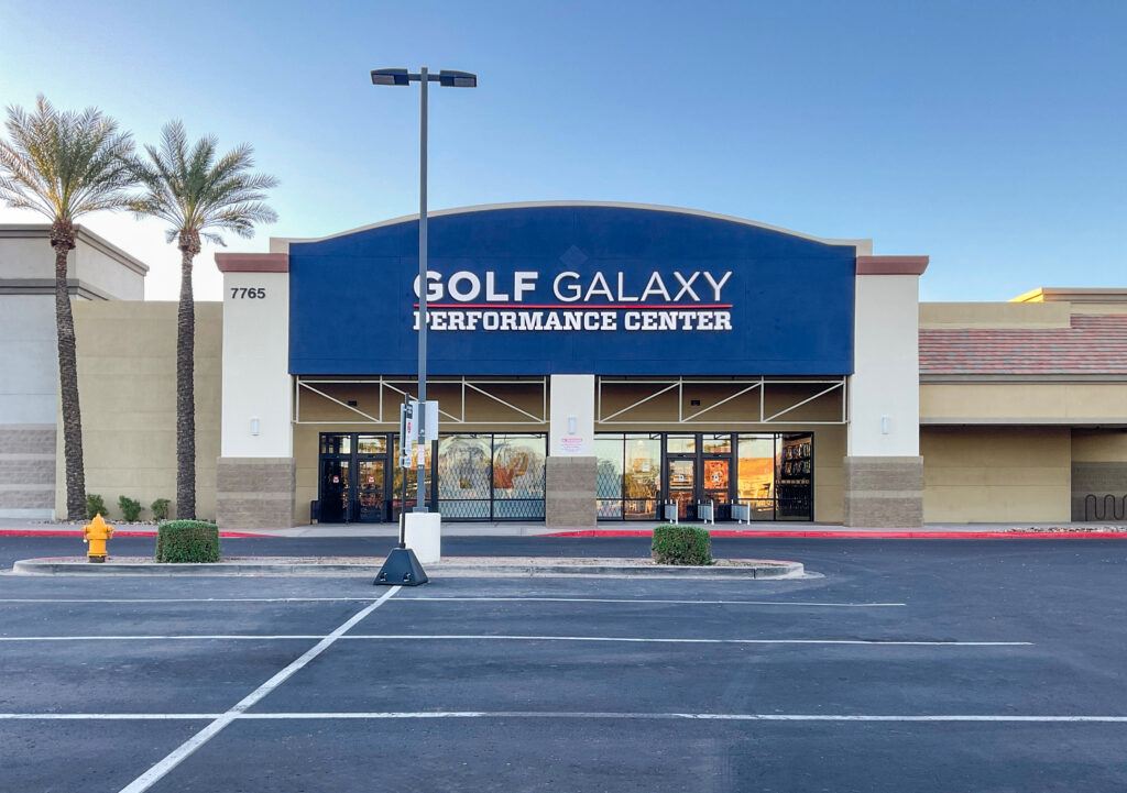 Exterior of a Golf Galaxy Performance Center store in a shopping plaza with a parking lot in the foreground.