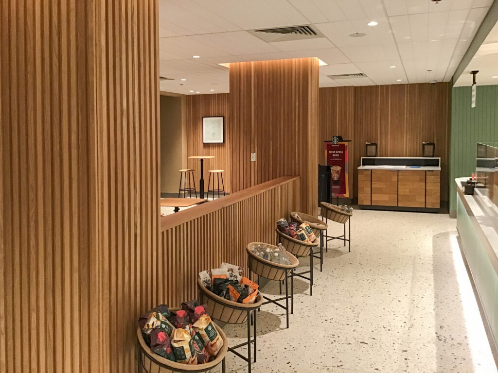 A row of metal baskets filled with packaged snacks and bottled drinks in a wood-paneled retail space.