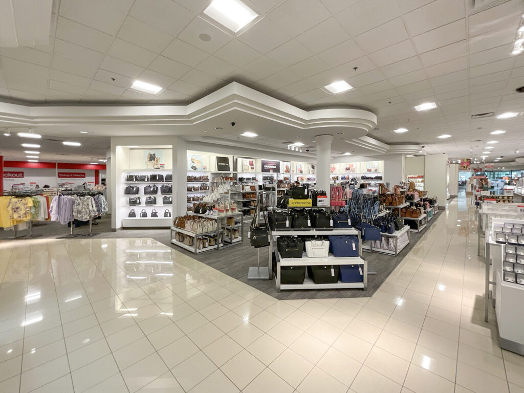 Interior of a department store featuring rows of shelves and displays filled with handbags.