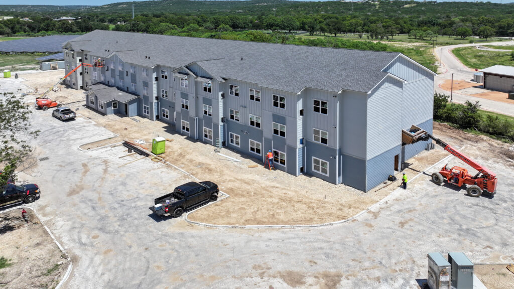 Aerial view of a multi-story apartment building under construction, featuring grey siding and several workers using aerial lifts on the site.