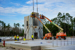 Construction workers on boom lifts install a concrete wall panel at a building site.