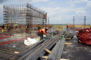 Construction workers on a building site working with rebar and red conduit pipes.