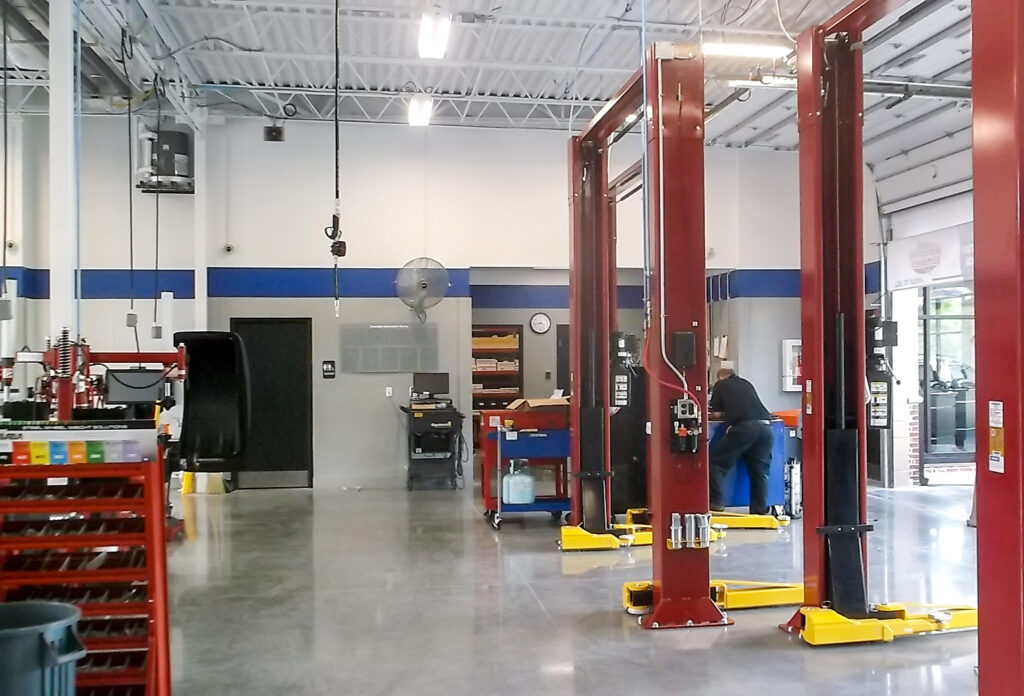 A mechanic working on a vehicle lifted by a red hydraulic hoist inside an auto repair shop.
