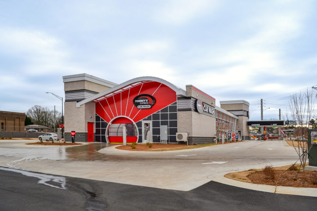 Tommy’s Express Car Wash building with a curved roof, red and black exterior, and entrance tunnel.