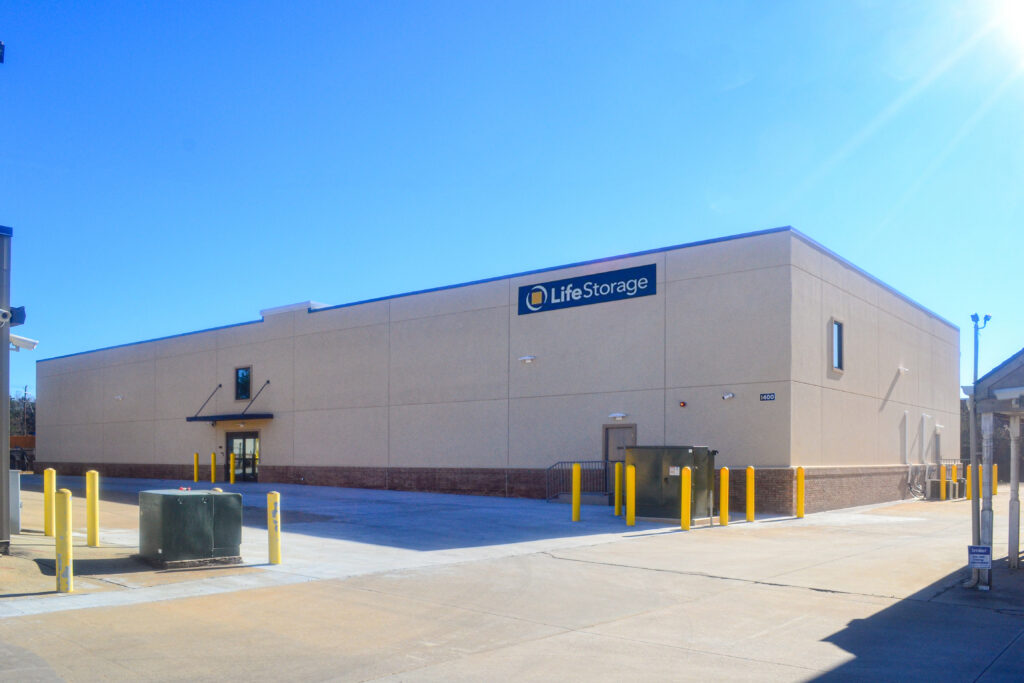 Exterior of a tan Life Storage building with a concrete parking lot and yellow bollards.