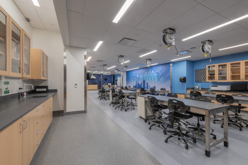 A science laboratory with rows of workstations, adjustable stools, and a blue accent wall featuring a skyline mural.