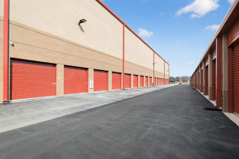 A long row of red self-storage unit doors along an asphalt driveway.