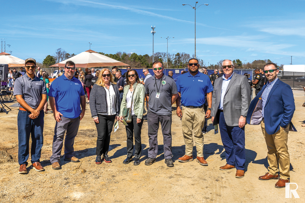 A group of seven adults standing in a line at an outdoor event on a dirt lot.