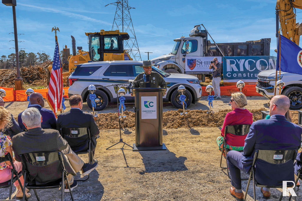 A person in a uniform speaks at a podium during a ground-breaking ceremony at a construction site.