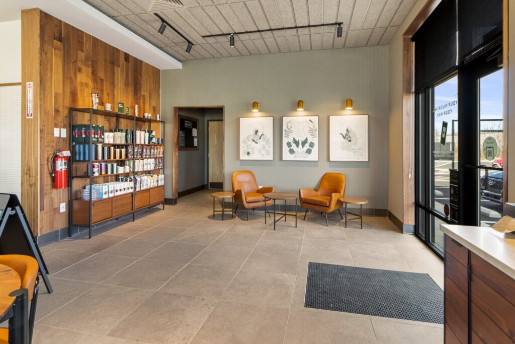 Lobby area with a retail shelf of merchandise, two leather armchairs with small tables, and three botanical art prints on the wall.