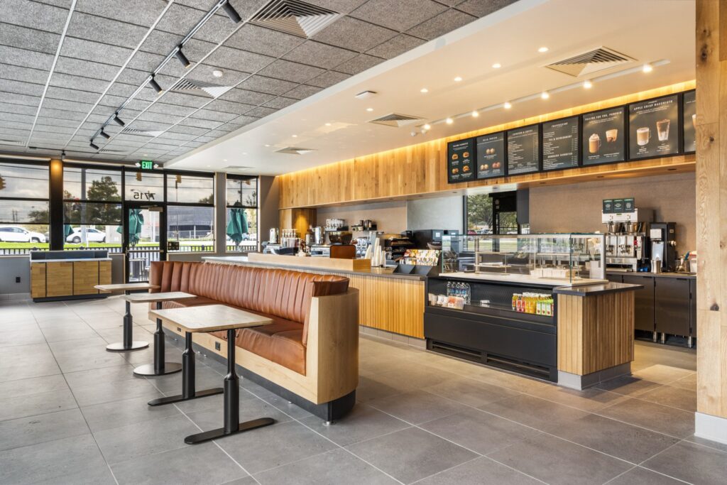 Interior of a modern coffee shop with a long brown leather bench, small tables, a service counter, and a menu board listing drinks and food.