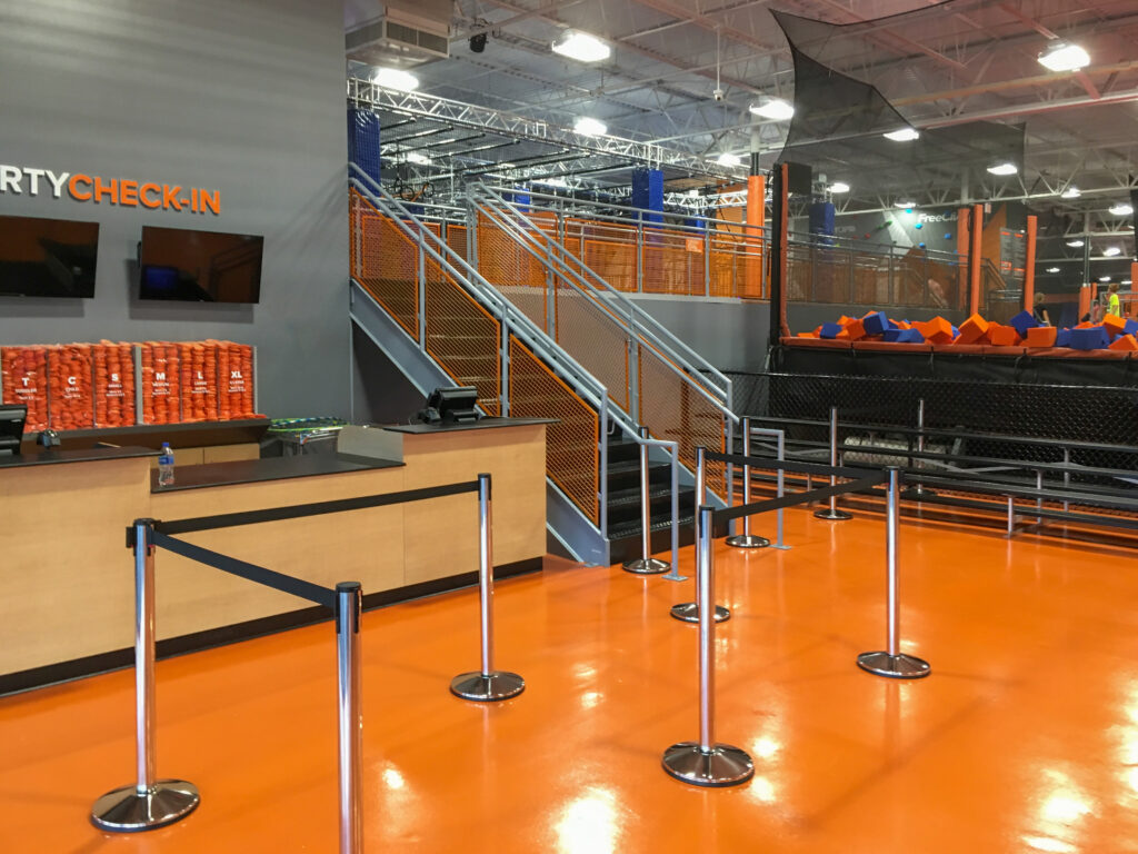 Party check-in counter at an indoor trampoline park with a queue line, stairs, and a foam pit.