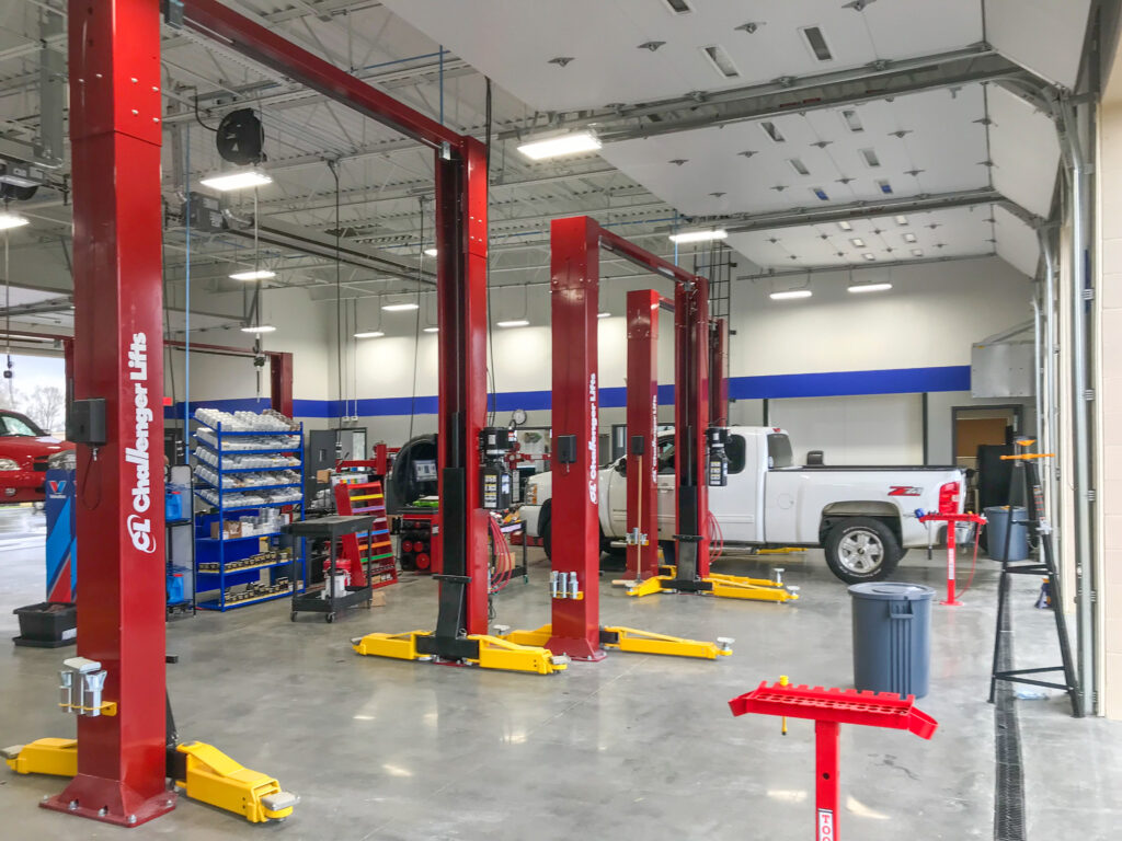 An auto repair shop interior featuring multiple red Challenger brand vehicle lifts and a white pickup truck.
