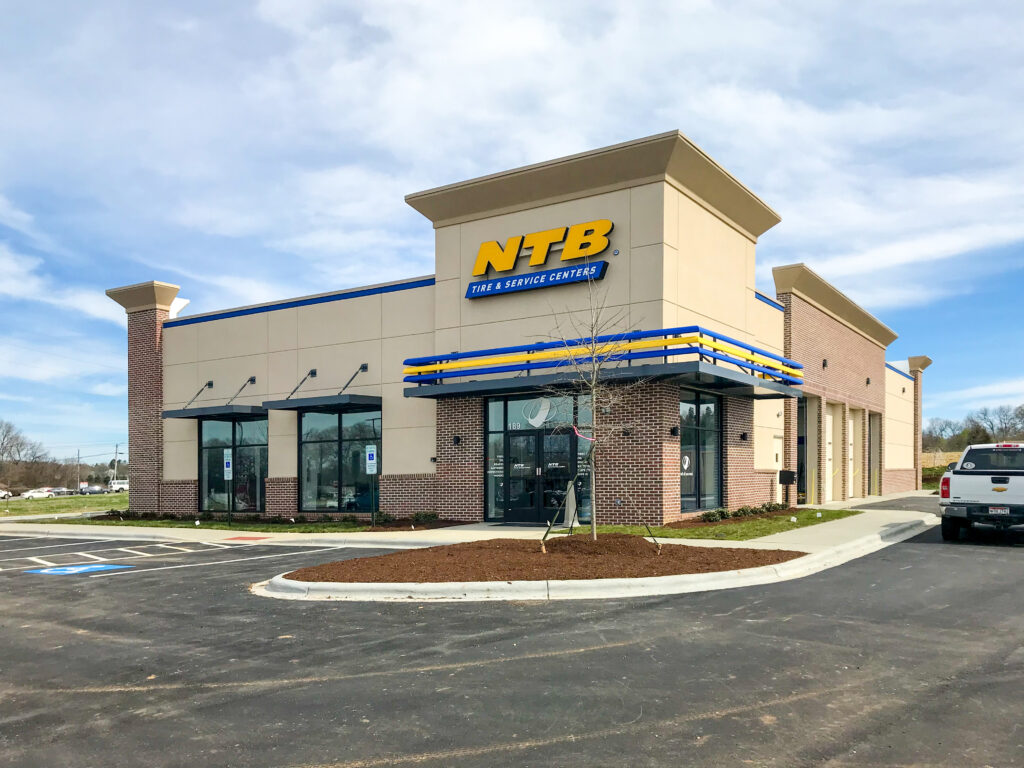Exterior view of an NTB Tire & Service Centers building with a parking lot and a pickup truck parked on the right.