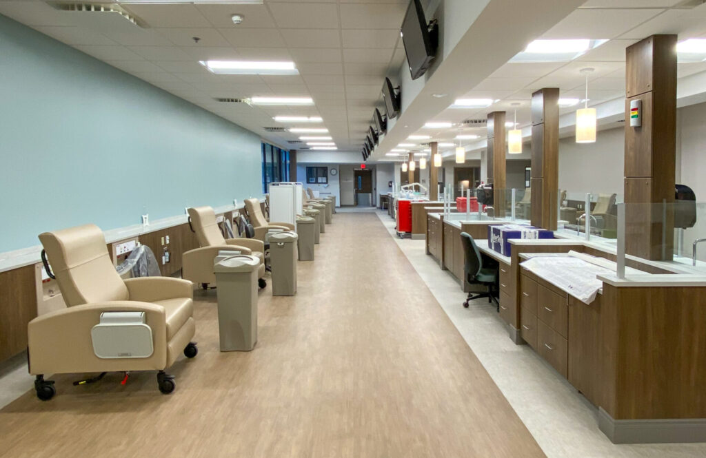 An infusion clinic interior with a row of reclining chairs on the left and nurse workstations on the right.