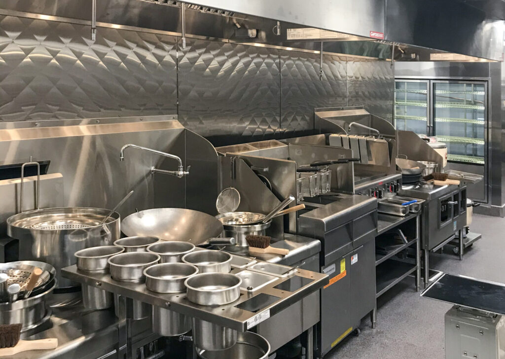Commercial kitchen line with stainless steel prep stations, deep fryers, and a wok burner.
