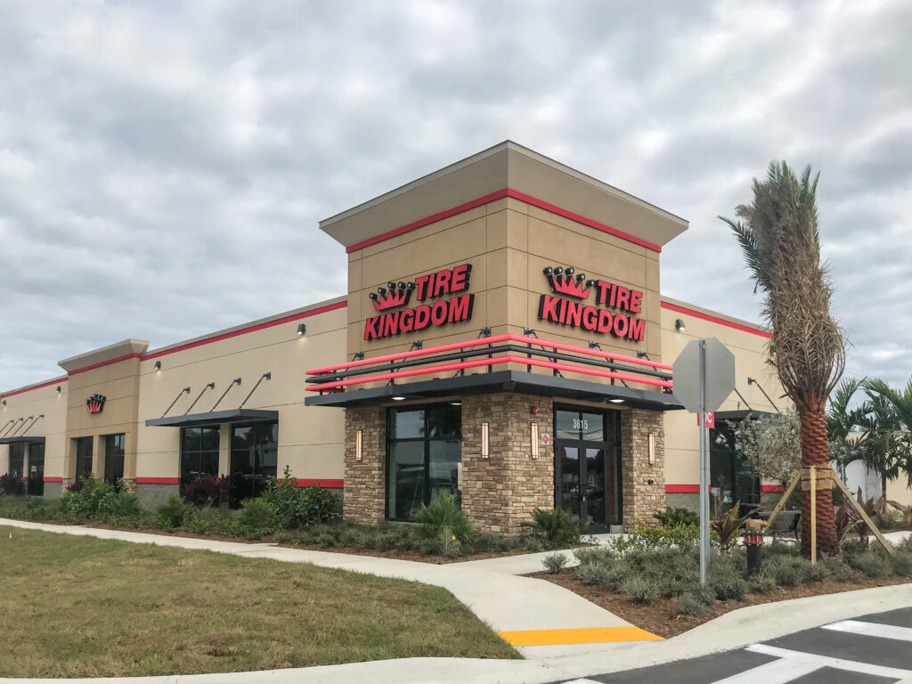 Exterior view of a Tire Kingdom store with beige walls, a stone-accented entrance, and a palm tree out front.