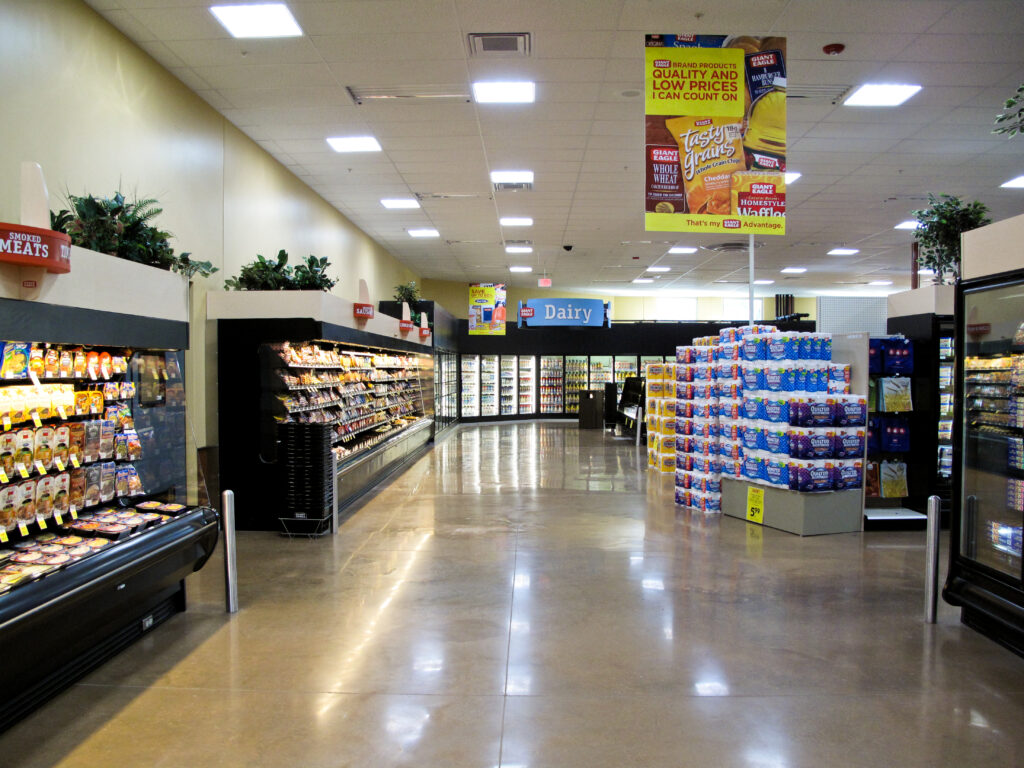 A grocery store aisle featuring refrigerated meat cases, a stack of paper towels, and a hanging advertisement for Giant Eagle brand products.