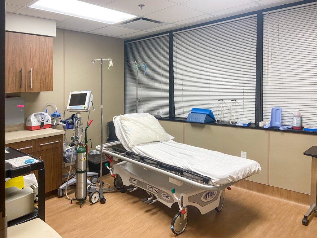 A hospital exam room with a gurney, a patient monitor, and an oxygen tank.