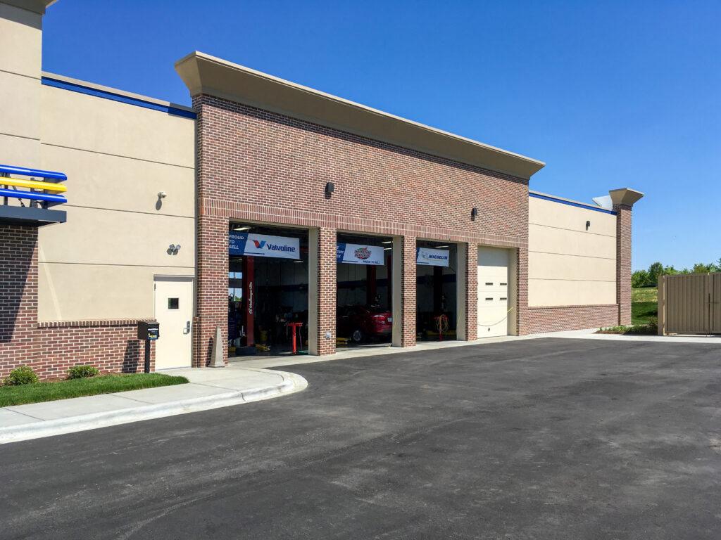 An auto service center exterior featuring three open garage bays under a brick and beige facade.