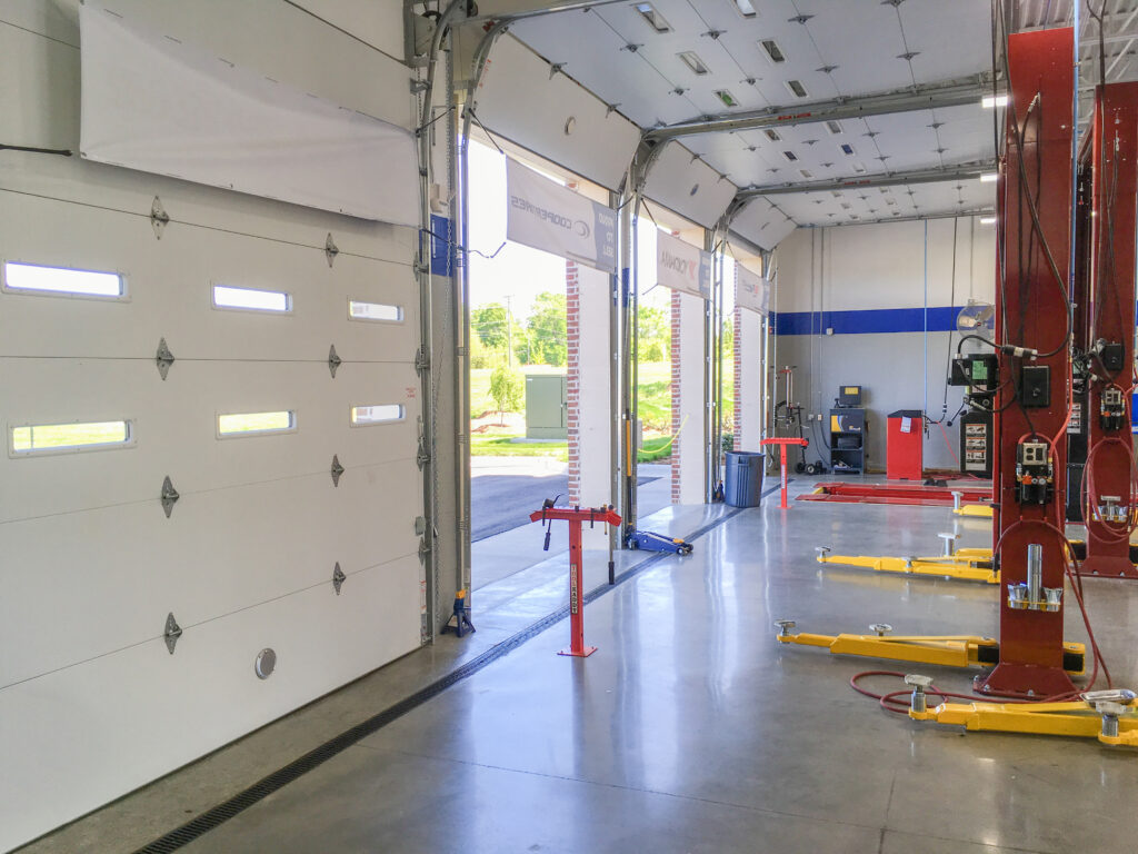 Interior of an auto repair shop with open bay doors and yellow hydraulic vehicle lifts.