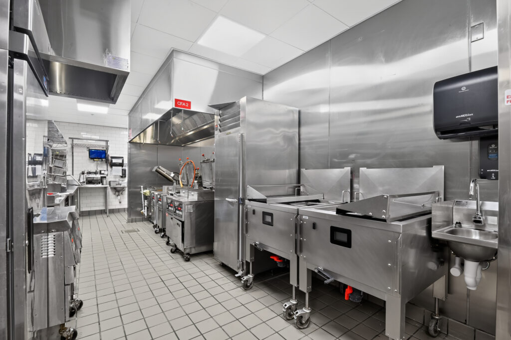 A commercial kitchen with stainless steel appliances, prep stations, and tiled floors.