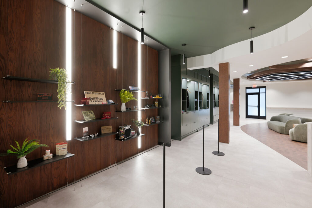 A retail showroom with open shelving displaying novelty signs and small gifts on a wood-paneled wall, leading to a seating area with curved sofas.