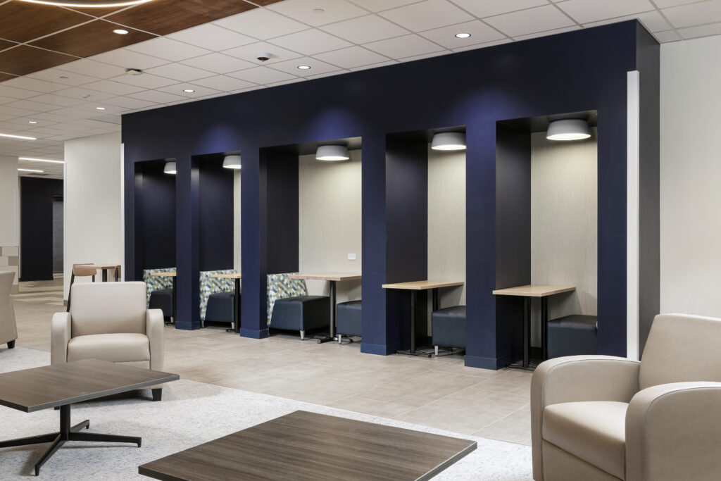A row of five recessed workspace booths with small tables and seating, positioned against a dark blue wall.