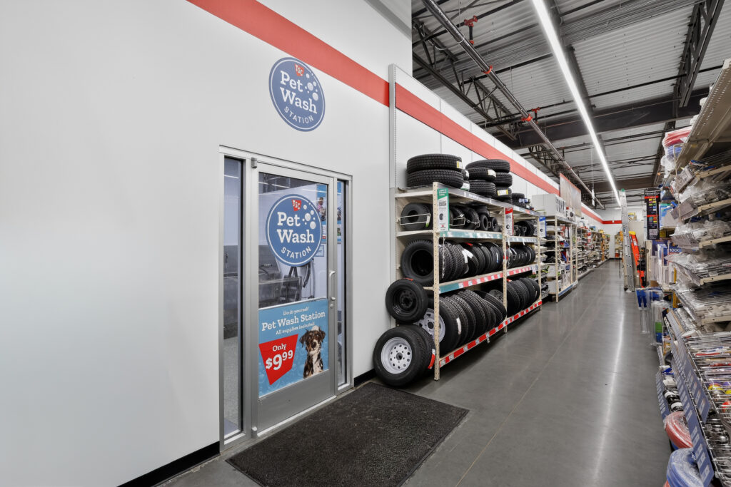 A store aisle featuring a pet wash station with a glass door and an adjacent shelving unit stocked with various tires.