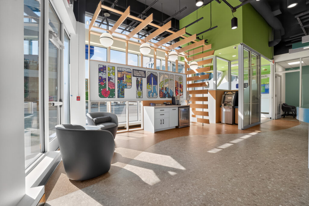 Modern office lobby with two gray armchairs, a white service counter, and a mural spelling “LIFE” on the wall.