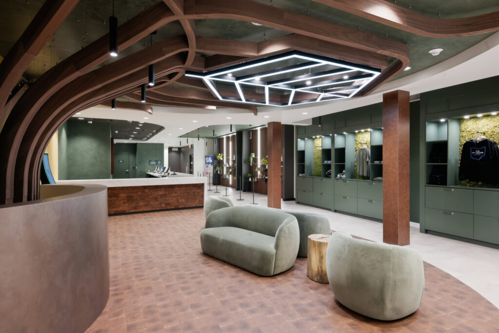 A modern lounge with sage green curved sofas, a reception desk, and a sculptural wooden ceiling feature.