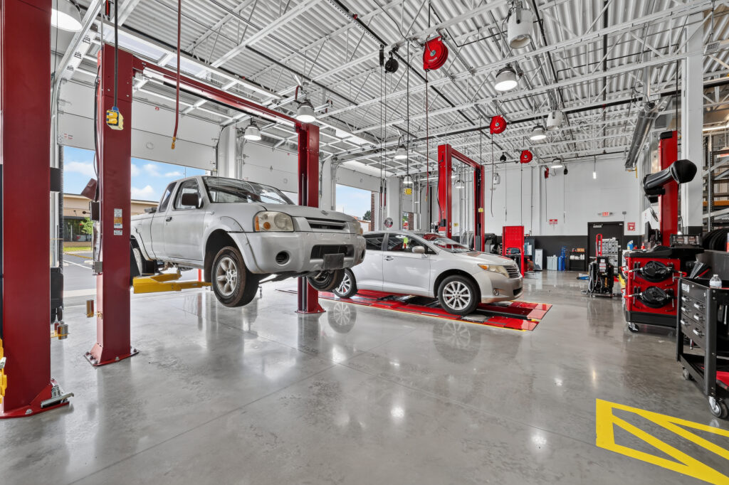 A silver pickup truck on a hydraulic lift and a silver sedan on an alignment rack inside a vehicle service center.