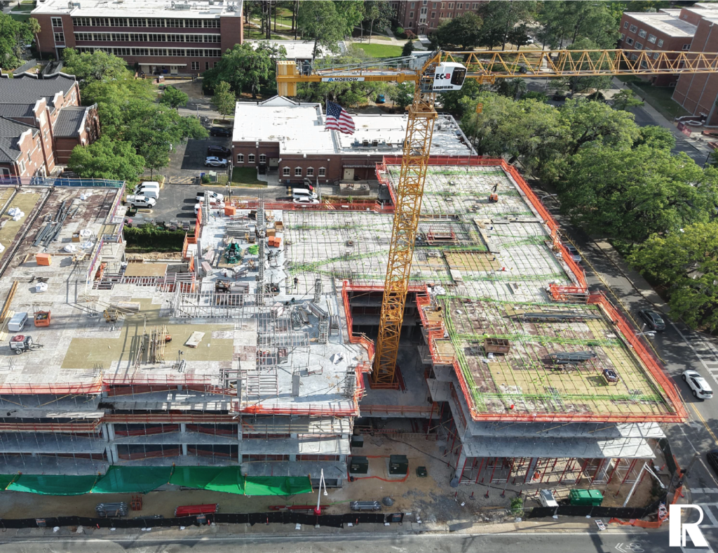 Aerial view of a multi-story building construction site with a yellow tower crane and an American flag.