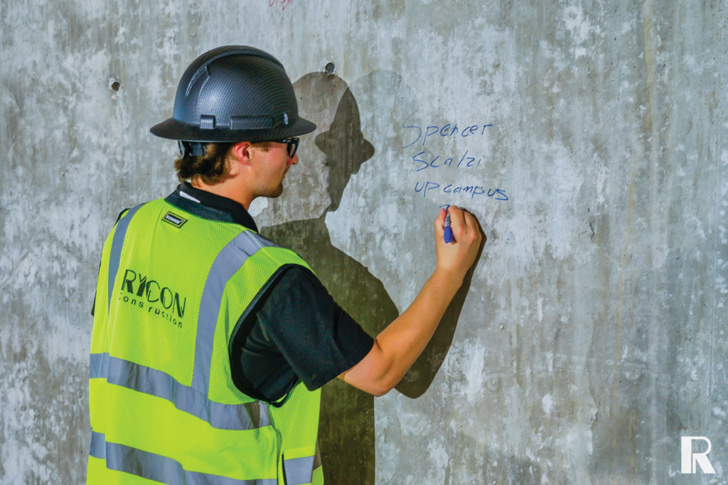 A construction worker in a hard hat and high-visibility vest writing on a concrete wall.