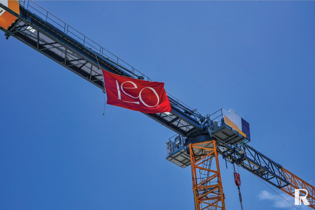 A red flag with the white text “LEO” hanging from the jib of a construction crane against a blue sky.