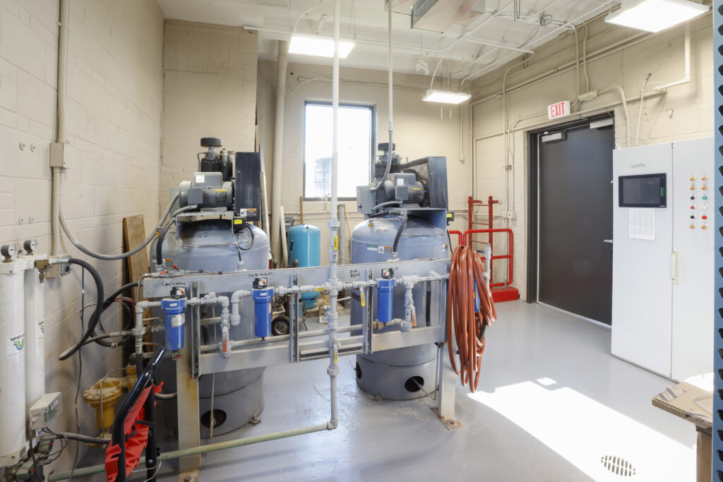 Two industrial air compressor tanks with attached piping and filter systems in a utility room.