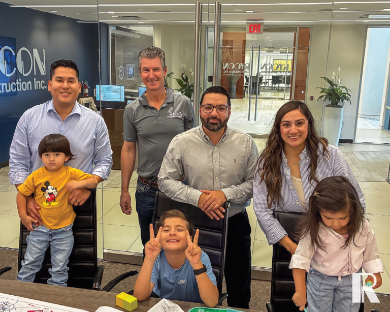 Four adults and two children in a modern office, with the Rycon Construction logo visible on the glass wall behind them.