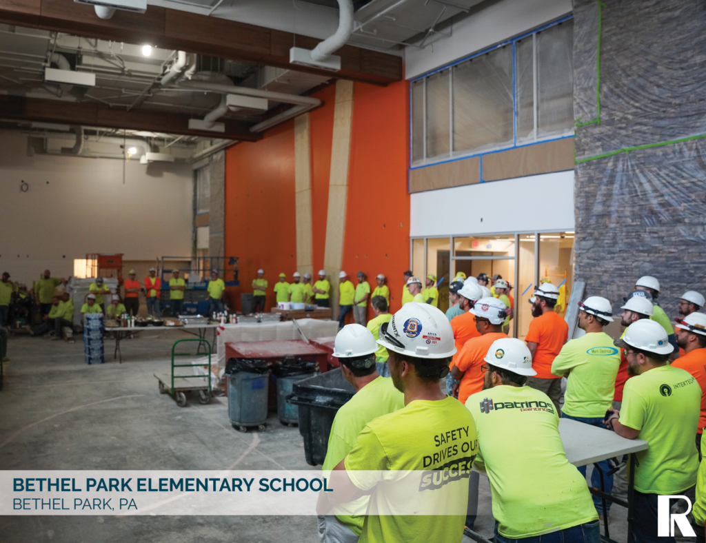 A group of construction workers in high-visibility shirts and hard hats attending a meeting inside a building under renovation.