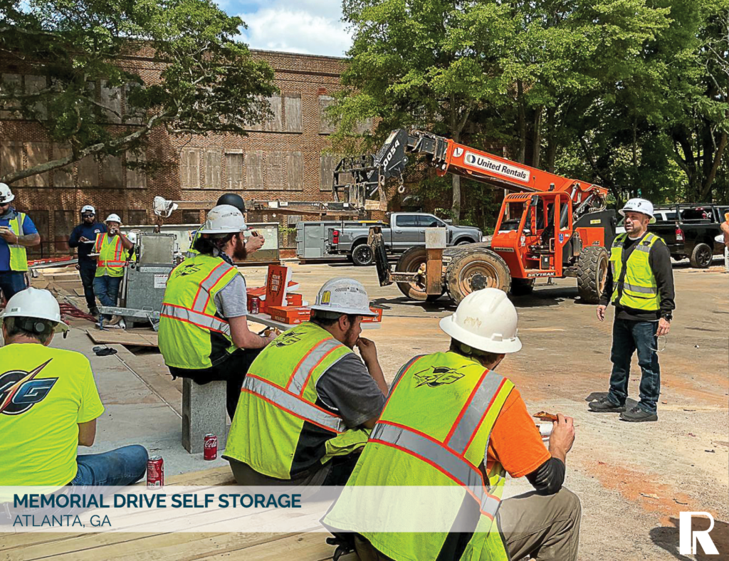 Construction workers in high-visibility vests take a break at a job site with an orange telehandler in the background. Text overlay reads: Memorial Drive Self Storage, Atlanta, GA.
