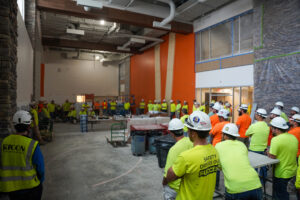 A group of construction workers in high-visibility shirts and hard hats gathered inside a building under construction.