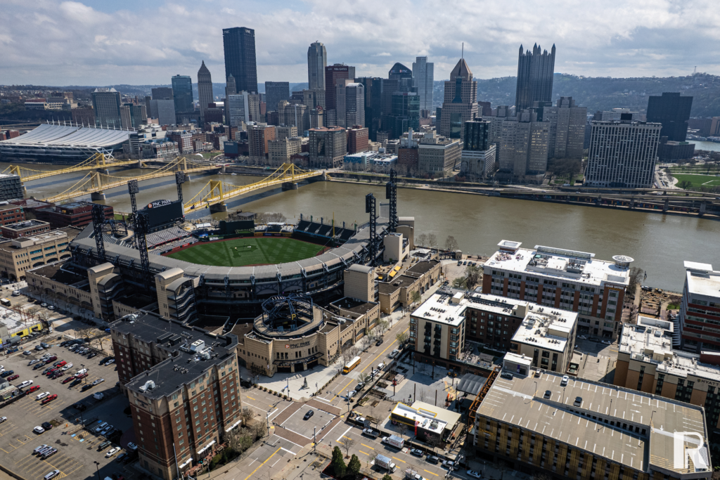 Aerial view of PNC Park baseball stadium, the Allegheny River with yellow bridges, and the Pittsburgh city skyline.