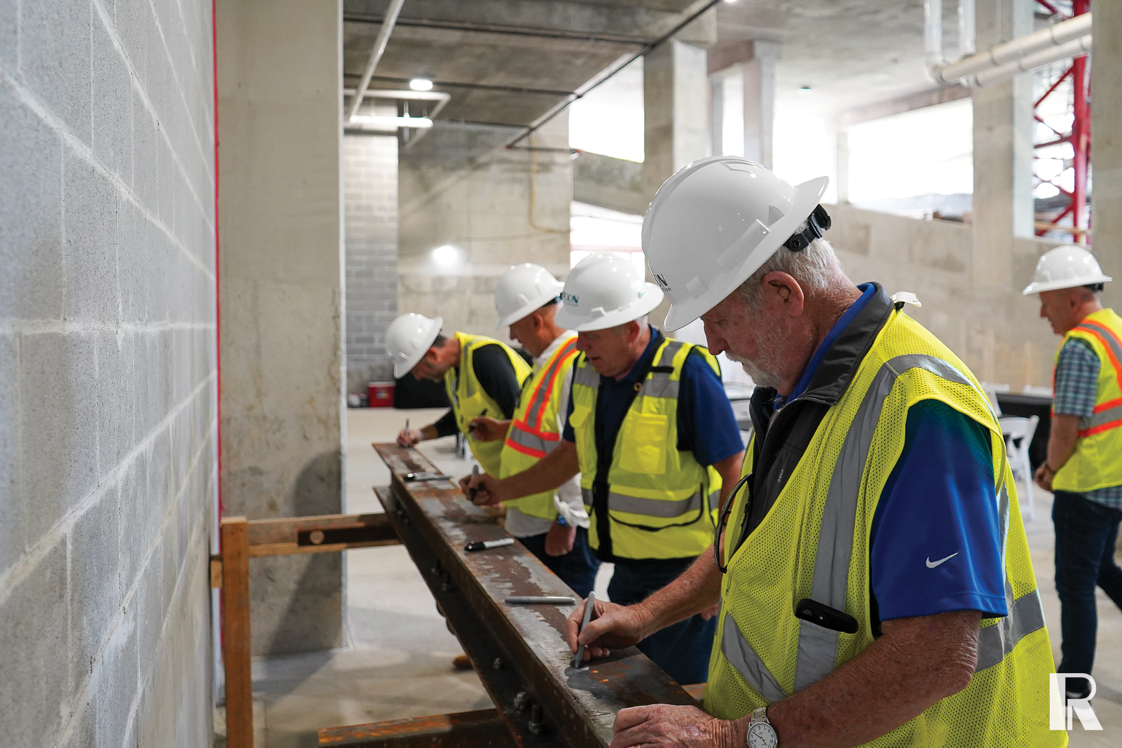 Four construction workers in hard hats and safety vests writing on a steel beam.