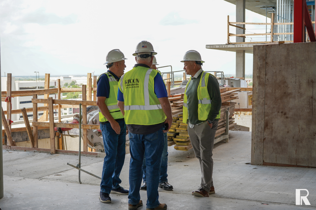 Three construction workers in hard hats and high-visibility vests standing on a building site and talking.