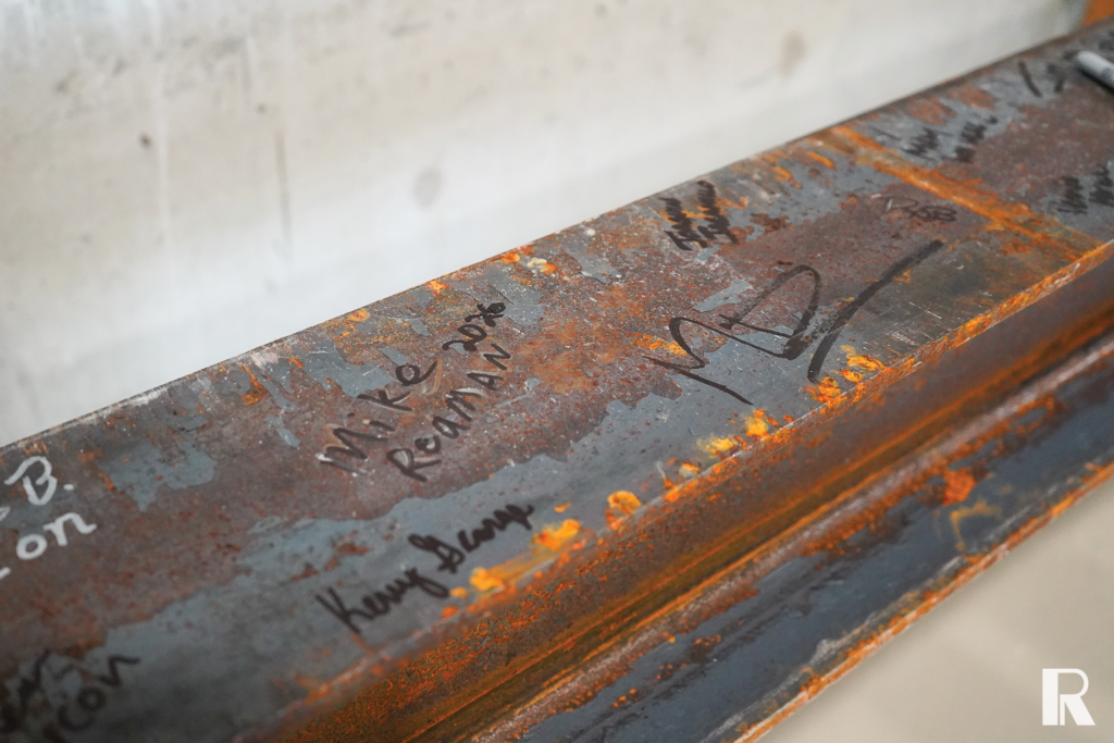 Rusted steel beam with several handwritten names and signatures in marker.