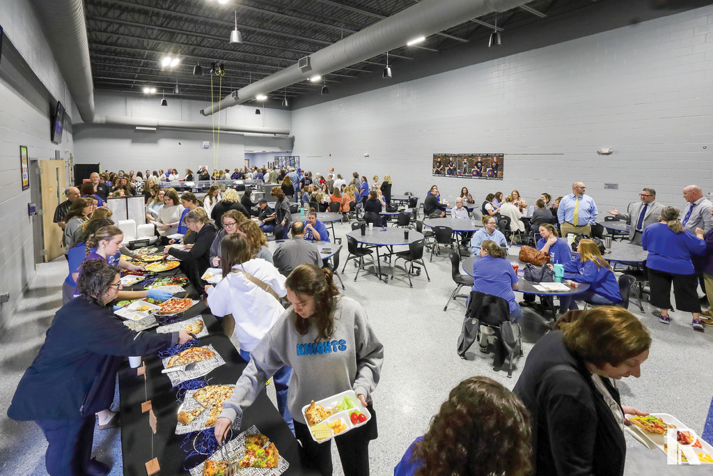 People gathering in a large cafeteria for a buffet-style meal.