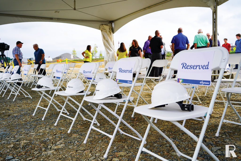 Rows of white folding chairs set up for an outdoor event, each with a white hard hat and a “Reserved” sign.